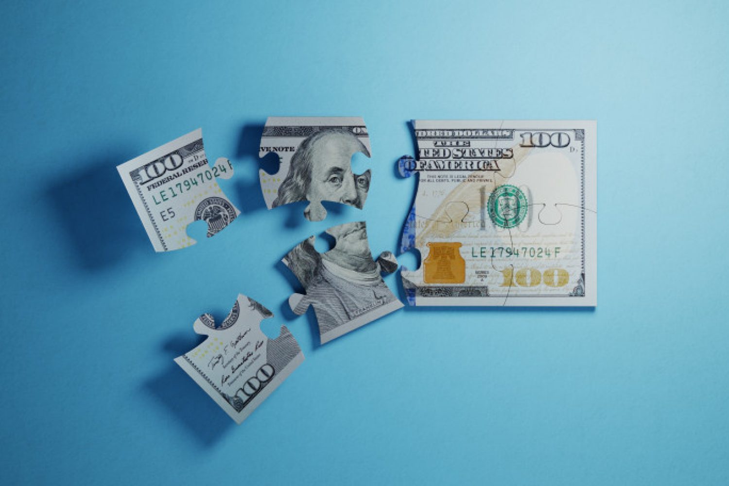 Jigsaw puzzle pieces textured with one hundred American dollar banknote on blue background. Horizontal composition with selective focus and copy space. Great use for American dollar currency and financial concepts.