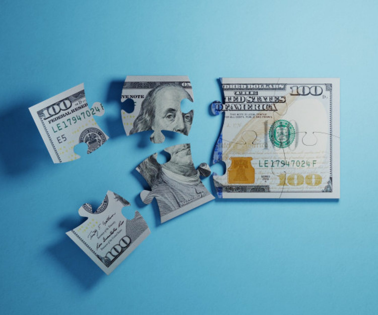 Jigsaw puzzle pieces textured with one hundred American dollar banknote on blue background. Horizontal composition with selective focus and copy space. Great use for American dollar currency and financial concepts.